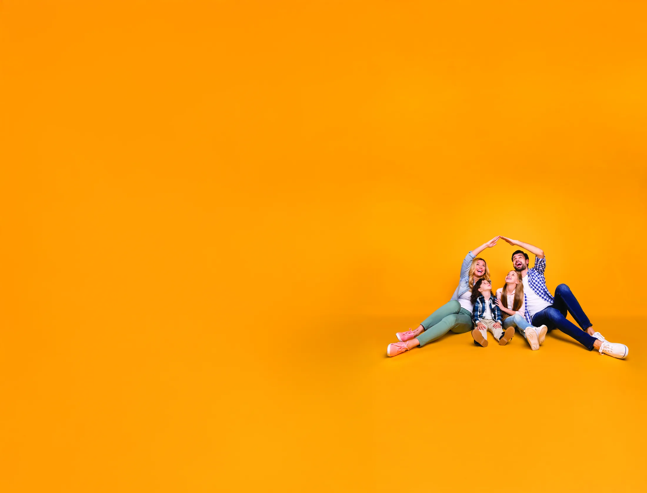 A happy New Zealand family sitting together, arms raised to form a roof over their heads